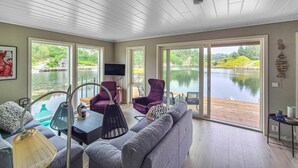 A spacious room with a grey sofa, purple armchairs, and a wooden table. Large windows offer views of a lake and greenery. - 5 bedroom gorgeous home in Bremnes (Bremnes)
