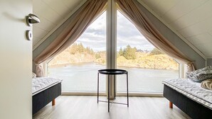 A bedroom with a large window, two beds, a small table, and a view of a lake and forest. - 5 bedroom gorgeous home in Bremnes (Bremnes)