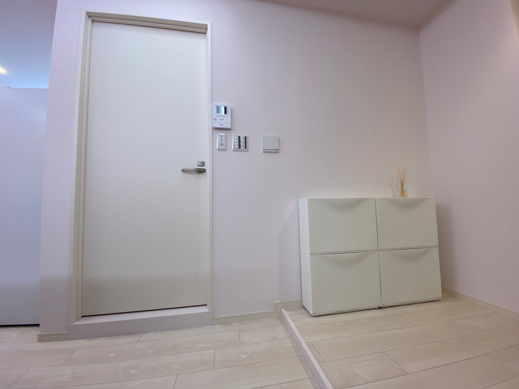 A room with a white door, a small white cabinet, and a light-colored floor.
