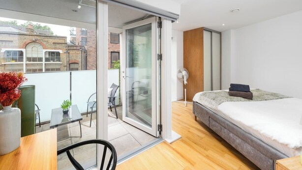A modern bedroom with a bed, a desk, and a sliding glass door leading to a balcony. - Shoreditch | 3 King Beds | Fast Wi-Fi | Balcony (London)