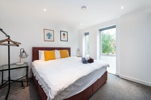 A modern hotel room with a large bed, a wardrobe, a bedside table, and a window with a view. - Shoreditch | 3 King Beds | Fast Wi-Fi | Balcony (London)