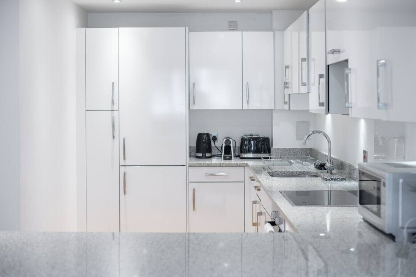 Une cuisine moderne avec des meubles blancs, un plan de travail en granit, une machine à café, un grille-pain et un évier.