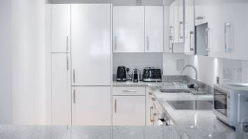 Une cuisine moderne avec des meubles blancs, un plan de travail en granit, une machine à café, un grille-pain et un évier.