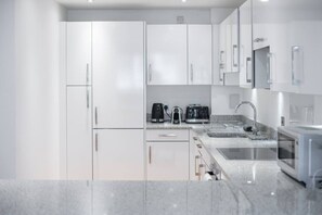 A modern kitchen with white cabinets, a granite countertop, a coffee maker, a toaster, and a sink. - Shoreditch | 3 King Beds | Fast Wi-Fi | Balcony (London)