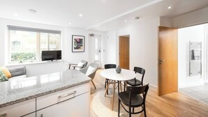 A modern kitchen with a granite countertop, a dining area with a round table and chairs, and a large window providing natural light. - Shoreditch | 3 King Beds | Fast Wi-Fi | Balcony (London)