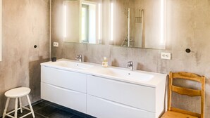 A bathroom with a double sink vanity, a mirror, and a wooden chair.
