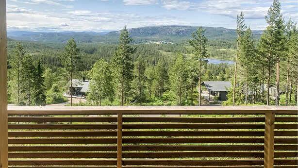 A wooden deck overlooking a mountainous landscape with dense forests and a lake.