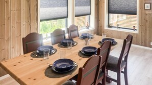 A dining table set with plates, glasses, and cutlery in a room with wooden walls and large windows.