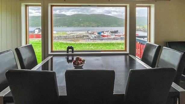 A dining area with a table and chairs, a bowl of fruit, and a view of a harbor with boats and a mountainous landscape. - Awesome home in Kongshus with sauna (Kongshus)