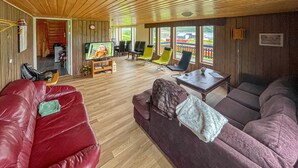 A spacious living room with a red leather sofa, a purple sofa, and a wooden coffee table. There is a television mounted on the wall, and the room has large windows offering a view of the outside. - Awesome home in Kongshus with sauna (Kongshus)