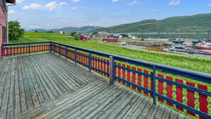 A wooden deck with a red and blue railing overlooking a marina with boats and a distant mountain range. - Awesome home in Kongshus with sauna (Kongshus)