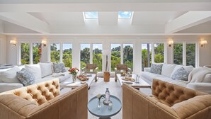 Ein großzügiger Wohnraum mit hoher Decke, großen Fenstern und einem zentral platzierten Couchtisch.