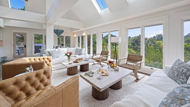 Ein geräumiges Wohnzimmer mit hohen Decken, großen Fenstern und Blick auf Grünflächen.