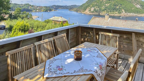 A wooden deck with a table and chairs, overlooking a river and hills. - 3 bedroom amazing home in Farsund (Farsund)