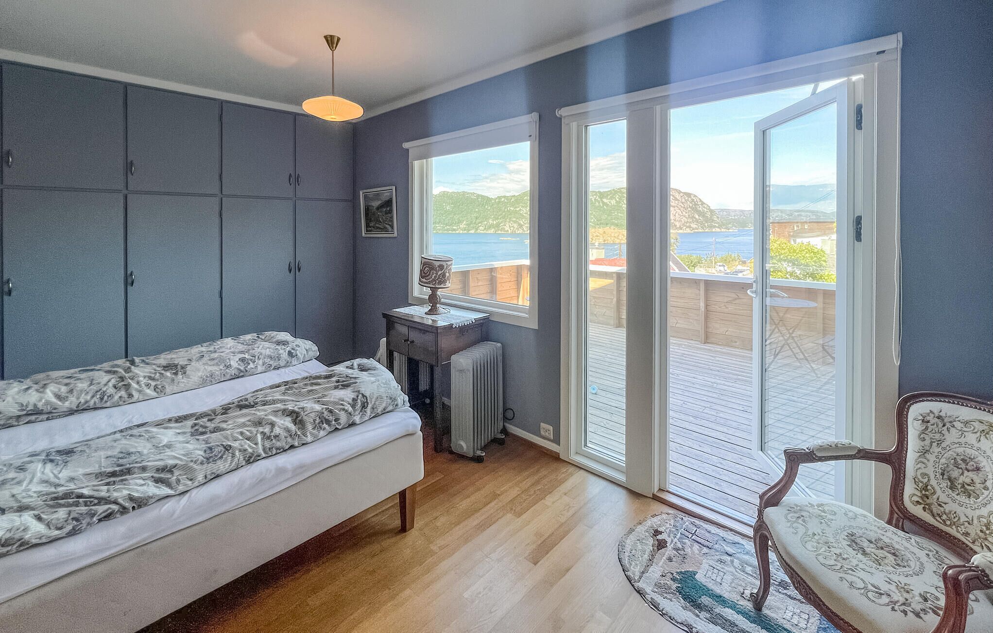 Ein Schlafzimmer mit Bett, Schminktisch, Heizkörper und Stuhl. Zwei Fenster bieten einen Blick ins Freie.
