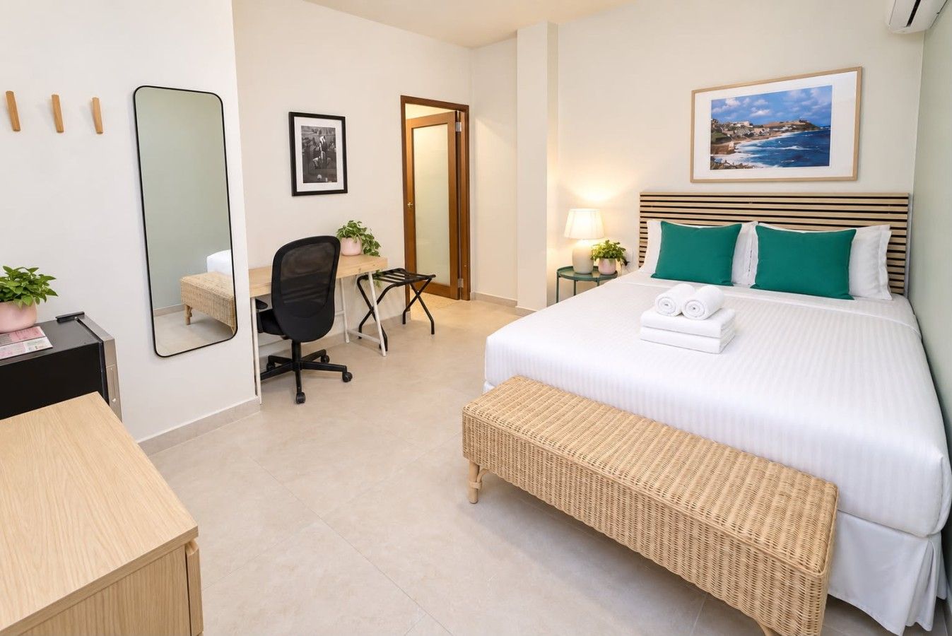 A hotel room with a bed, a desk, a chair, a mirror, and a picture on the wall.