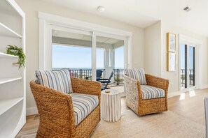 Un balcón con mobiliario de mimbre, piso blanco y vista al océano.
