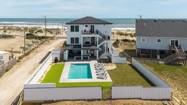 A two-story house with a pool, a balcony, and a view of the beach.