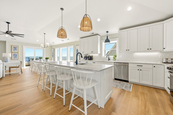 Una cocina moderna con armarios blancos, una isla central con taburetes altos e iluminación colgante, y vistas al exterior.