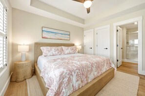 A bedroom with a bed, bedside lamps, a ceiling fan, a painting, and a bathroom door.