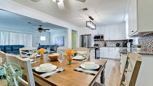 Une cuisine spacieuse avec des meubles blancs, un coin repas avec une table en bois dressée pour quatre personnes, et un salon avec un canapé bleu.