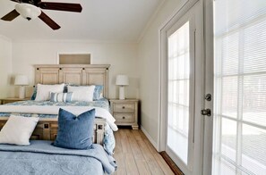 A bedroom with a bed, nightstands, a ceiling fan, and a large window.