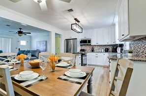 A spacious kitchen with white cabinets, a dining area with a wooden table set for four, and a living room with a blue sofa.