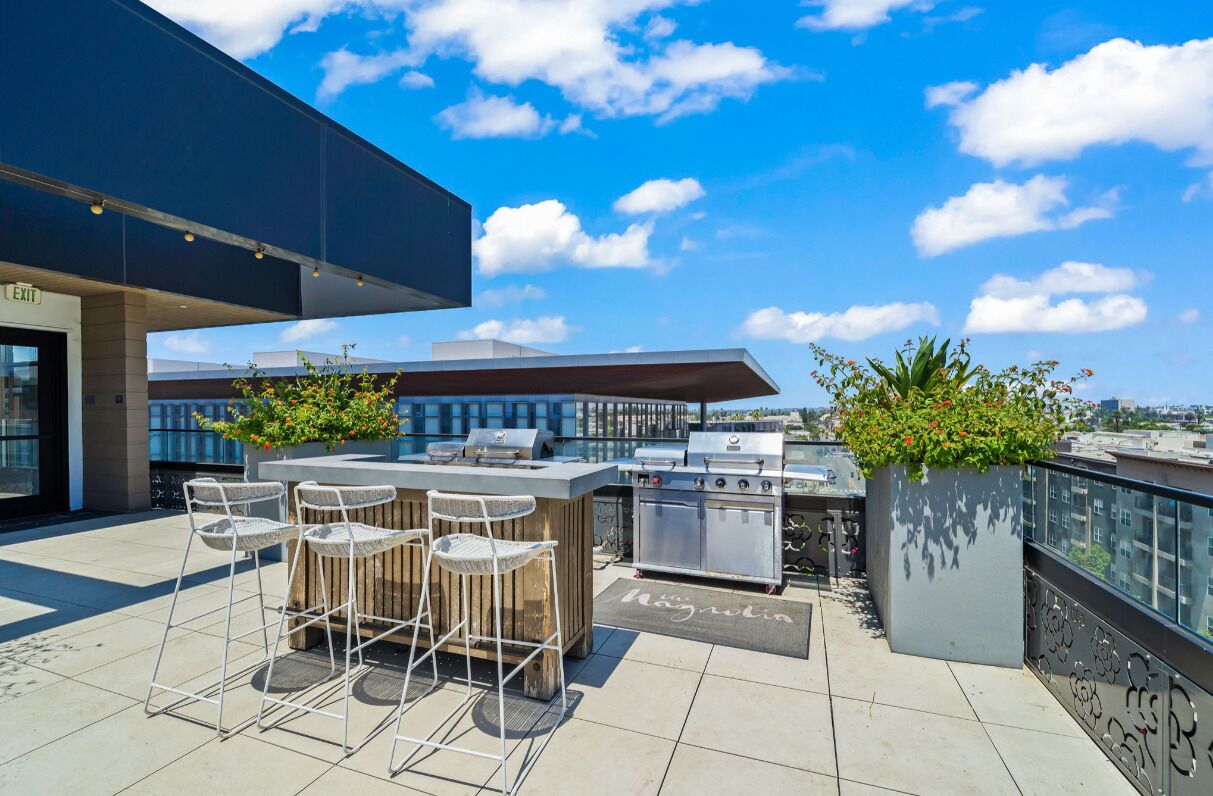 A rooftop bar with a grill station, outdoor seating, and potted plants.