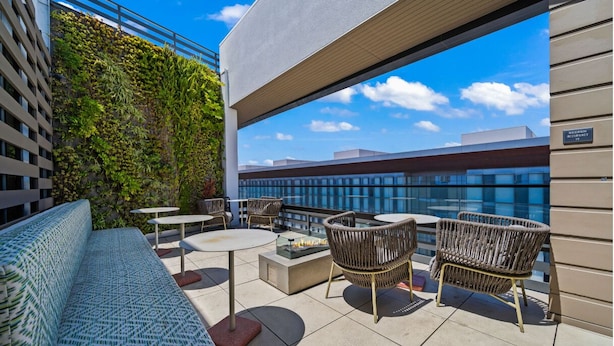 A rooftop terrace with a sofa, chairs, and tables, overlooking a cityscape.
