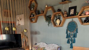 Een knus ingerichte kamer met een bed, een bank, een televisie, en een wand versierd met honingraatplanken en een dromenvanger.