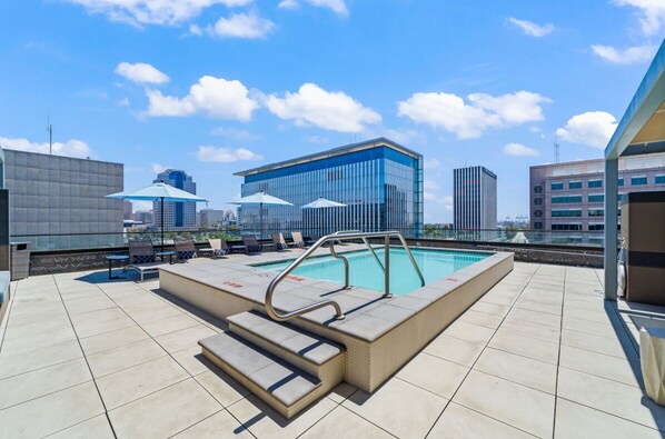 A rooftop pool area with lounge chairs, umbrellas, and a pool with steps leading into it. - Stylish Condo / Mins to Shoreline (Long Beach)