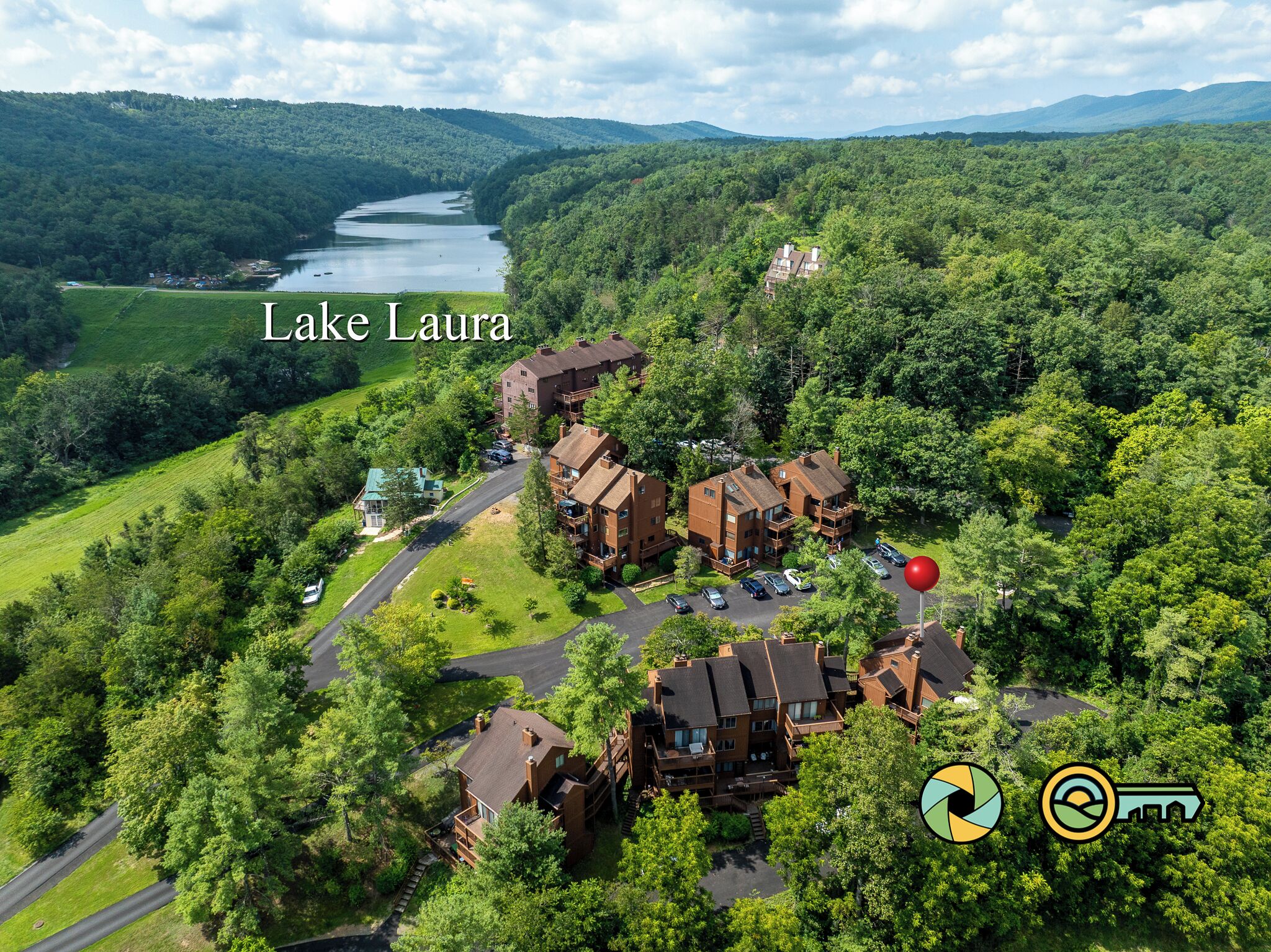 An aerial view of a lakeside resort with multiple buildings, a parking area, and a river in the background.