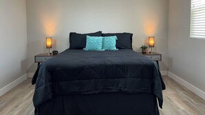 A bedroom with a dark-colored bed, two bedside lamps, and a window with blinds.
