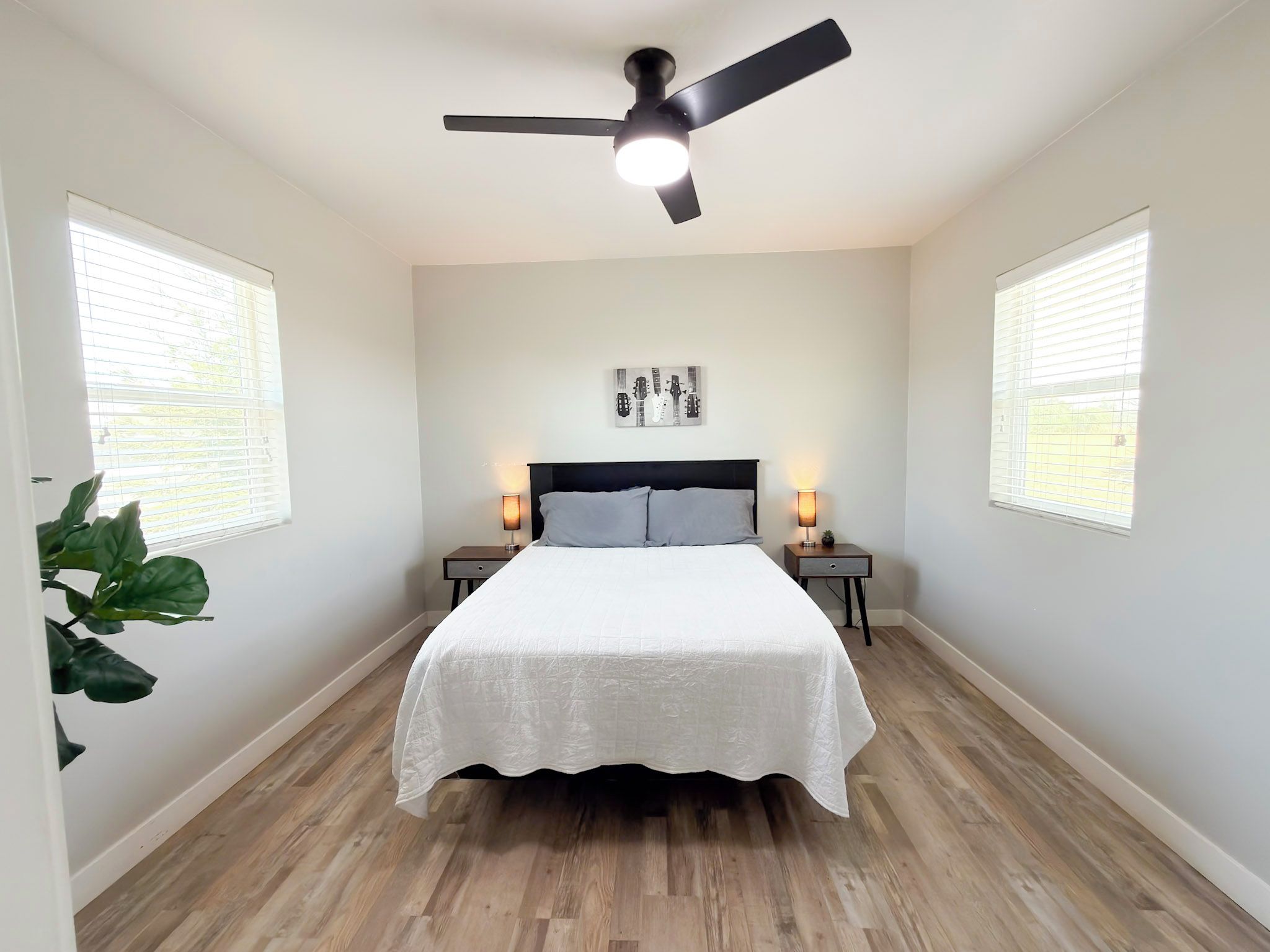 A bedroom with a bed, two bedside tables, a ceiling fan, and a window with blinds.
