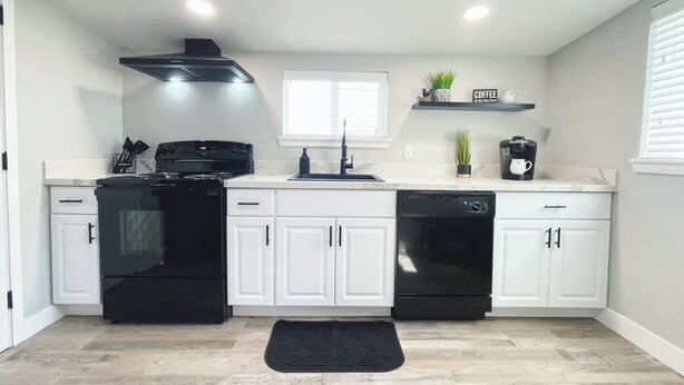 A modern kitchen with white cabinets, black appliances, a window, and a coffee station.