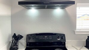 A kitchen with a black stove, a digital oven control panel, and a stainless steel range hood.