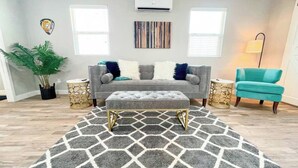 A living room with a grey sofa, a teal armchair, a patterned rug, and a potted plant.