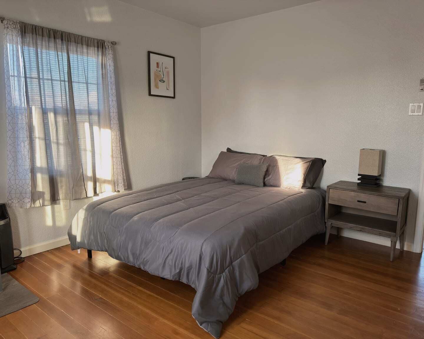 A bedroom with a bed, wooden nightstand, and a framed picture on the wall.