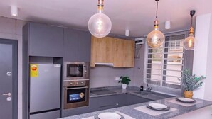 A modern kitchen with grey cabinets, a built-in oven, a microwave, and a large island with a granite countertop. - Harmony Heights (Tema)