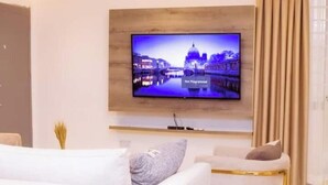 A modern living room with a flat-screen TV mounted on the wall, a white sofa, and a small side table. - Harmony Heights (Tema)