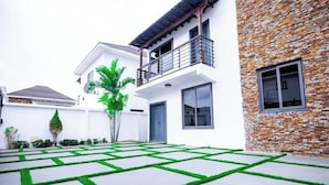 Une maison moderne avec une façade en pierre, un balcon et un jardin bien entretenu doté d’un pavage aux motifs géométriques.