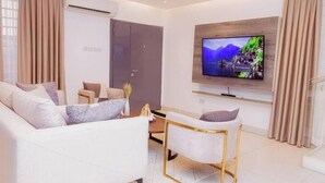 Un salon moderne avec un canapé, un fauteuil et un téléviseur à écran plat fixé au mur.