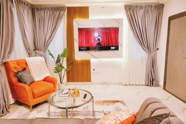 A living room with a sofa, a coffee table, a TV mounted on the wall, and curtains.