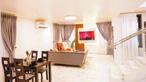 A modern living room with a dining area, a sofa, and a TV mounted on the wall. - Solace Villa (Tema)