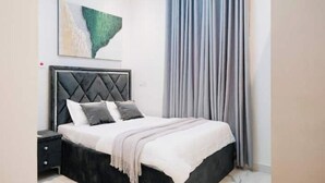 A bedroom with a bed, a nightstand, a wall-mounted artwork, and a window with curtains. - Maple Hill (Tema)