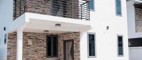 A two-story building with a balcony, a stone facade, and a tiled patio.