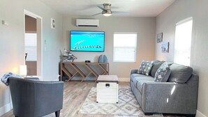 A living room with a grey sofa, a grey armchair, a wooden coffee table, and a TV on the wall.