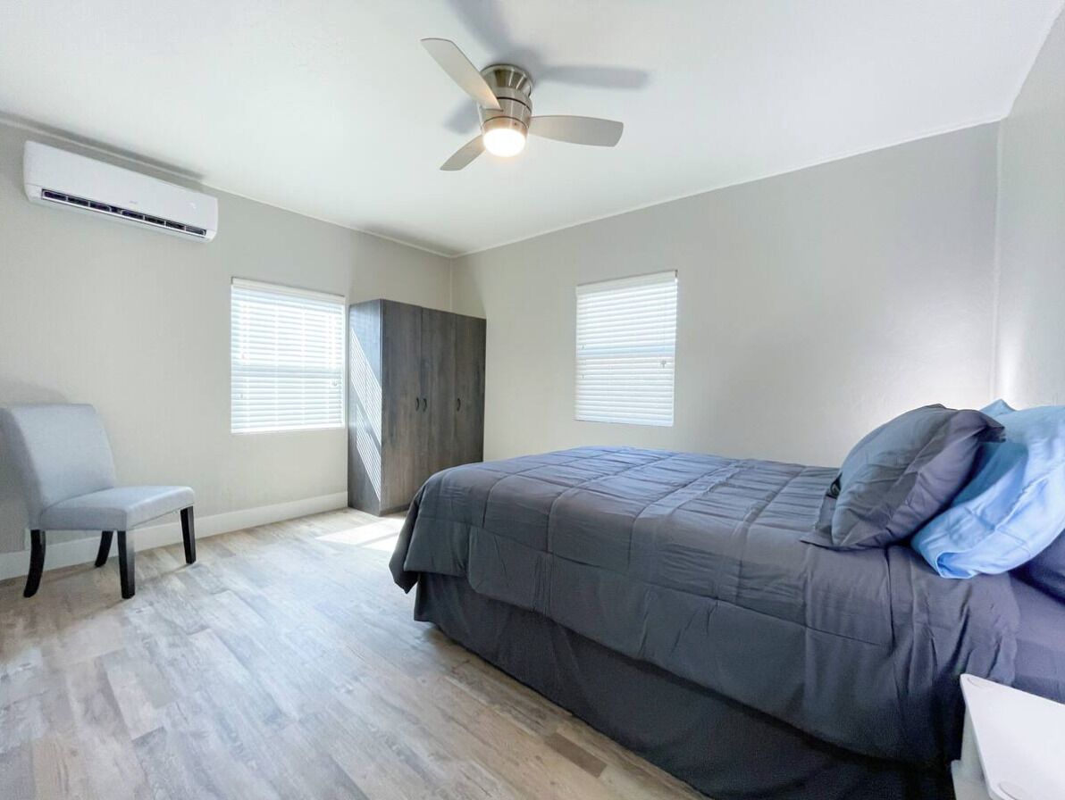 A bedroom with a bed, a chair, a ceiling fan, and two windows.