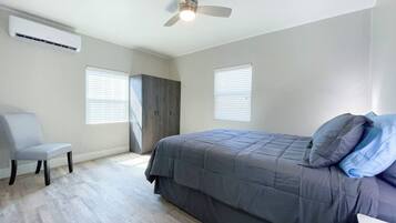 A bedroom with a bed, a chair, a ceiling fan, and two windows.