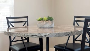 A round table with a marble top, two black chairs, and a potted plant in the center.